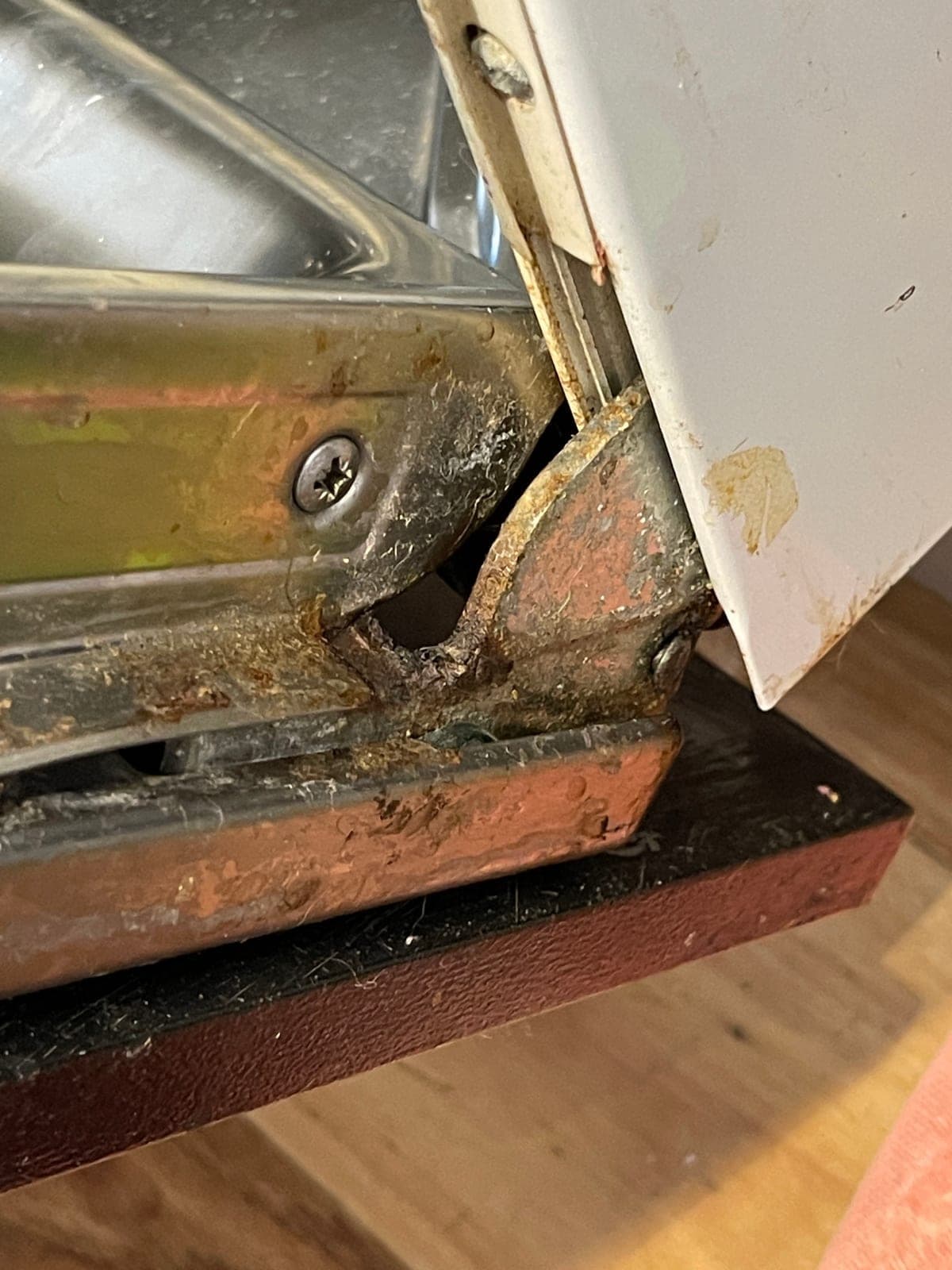 Rust and grime built up along the door frame of a dishwasher that has not been cleaned, wearing at the hinges.