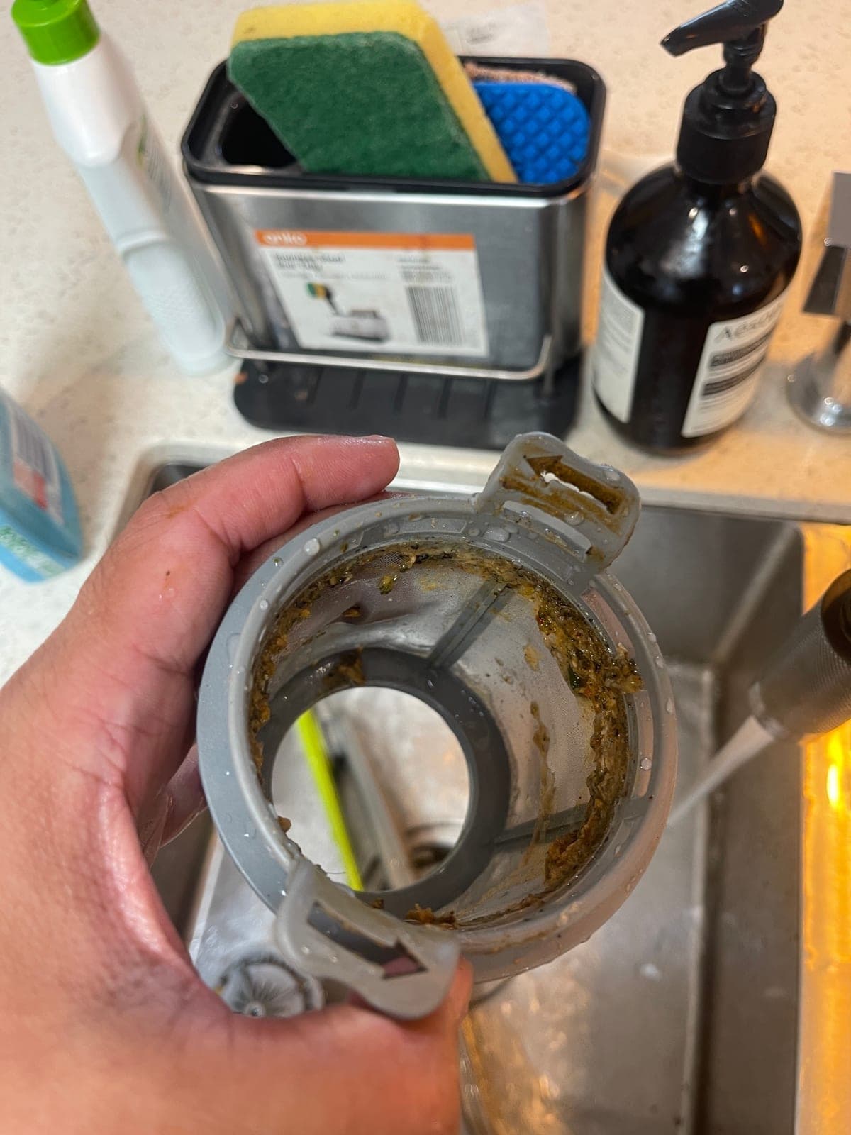 A blocked dishwasher filter held over the sink before cleaning.