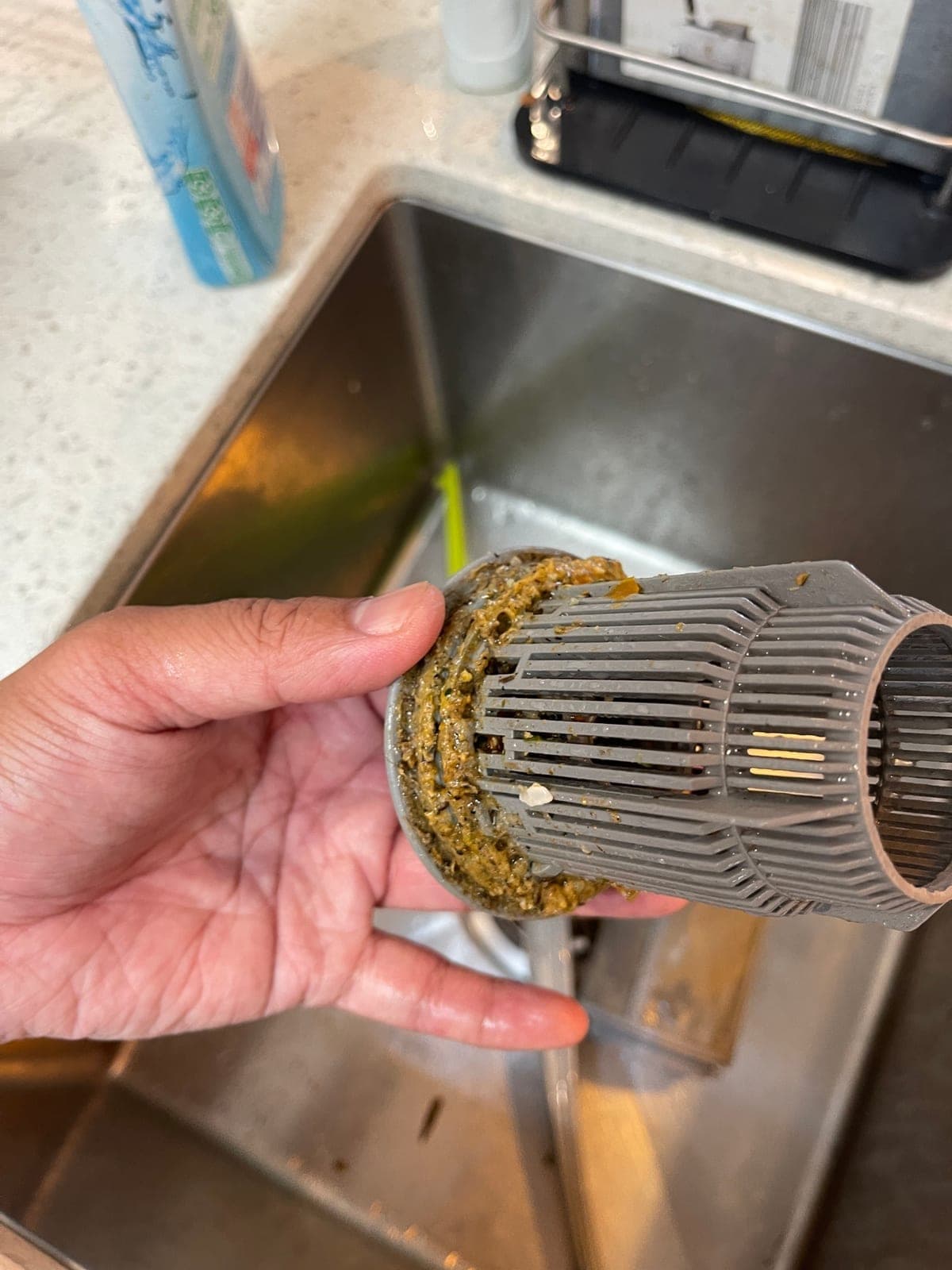 A dishwasher filter cylinder held up, coated in food waste.