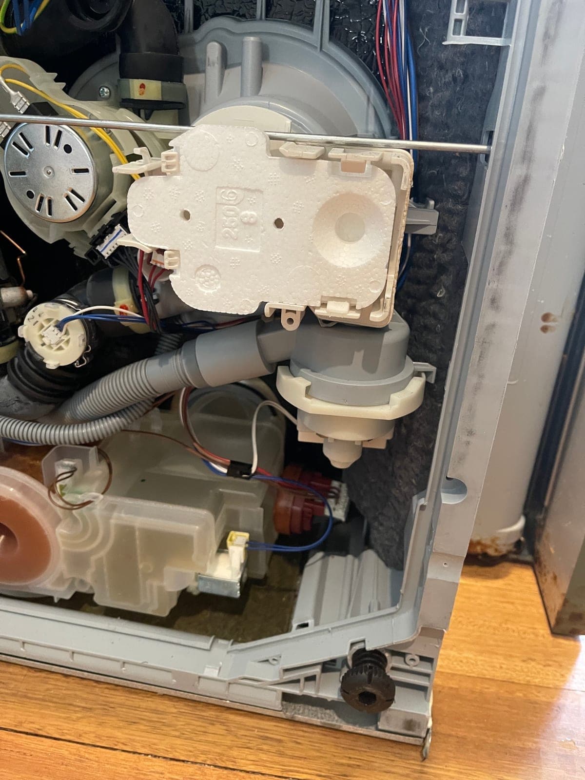 A dishwasher on its back with the base plate off, exposing the pump and hoses.