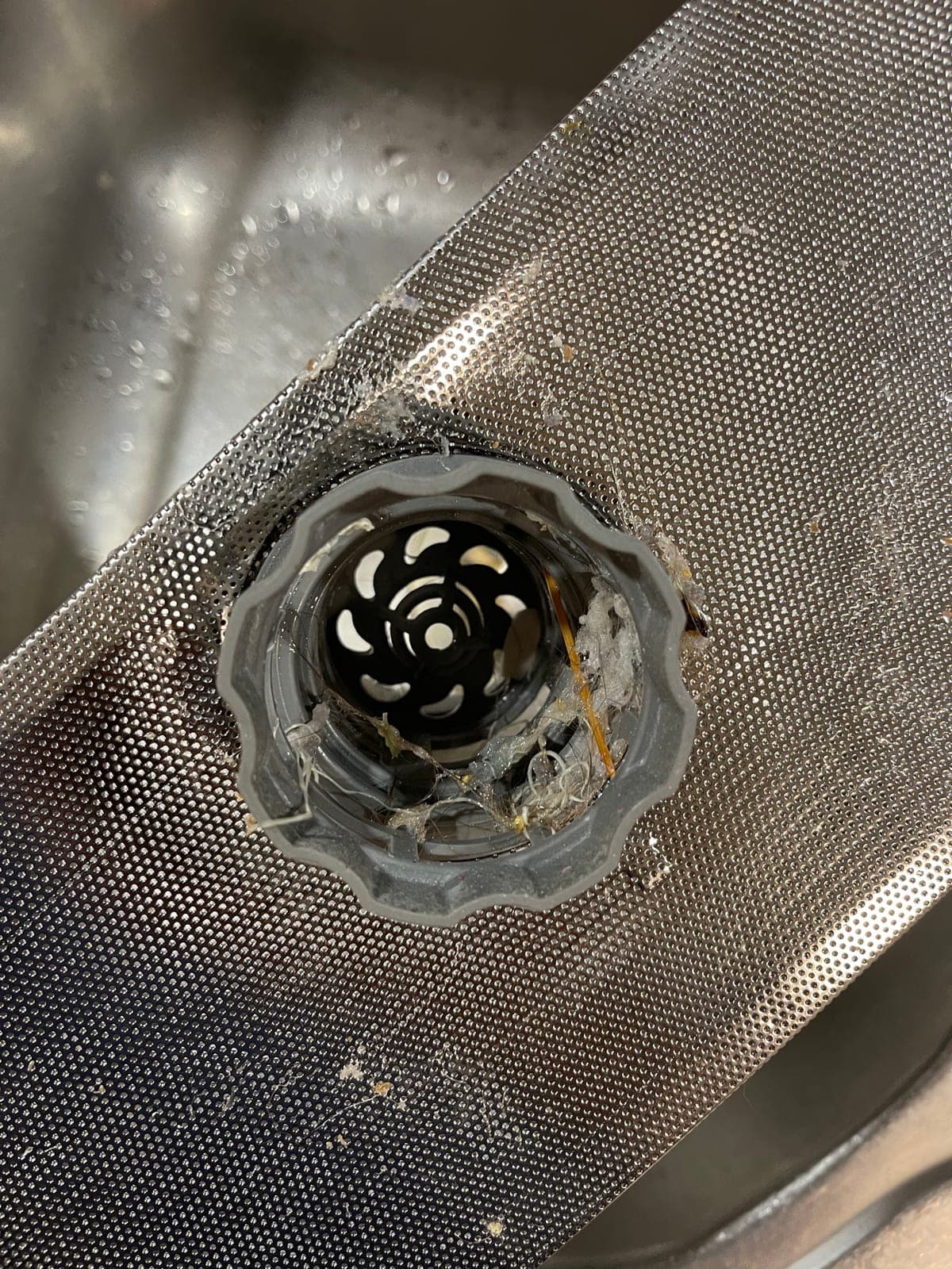 The sump grille of a dishwasher blocked with cooked-on residue.