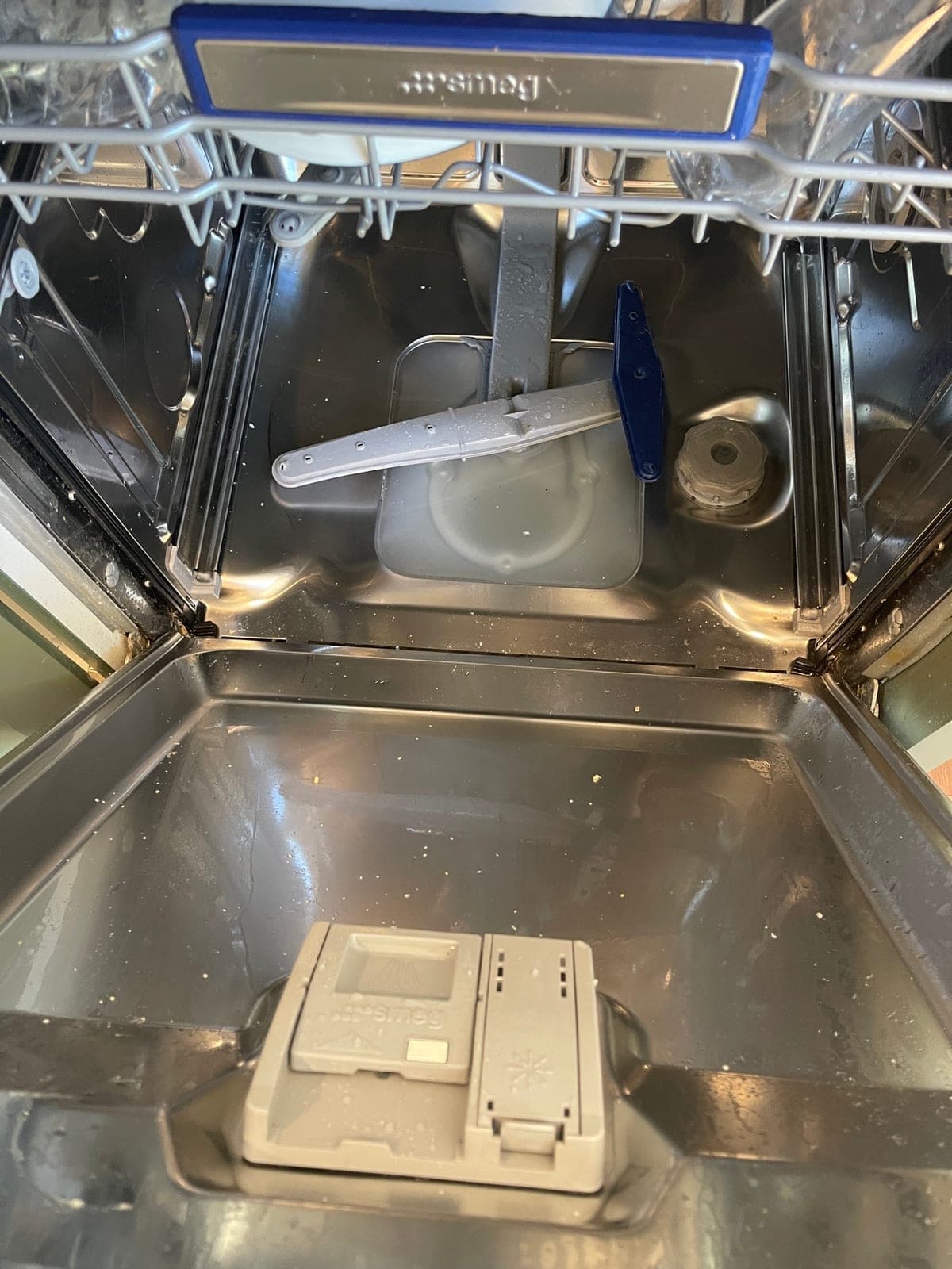 A dishwasher tub interior after cleaning, with the spray arms refitted.