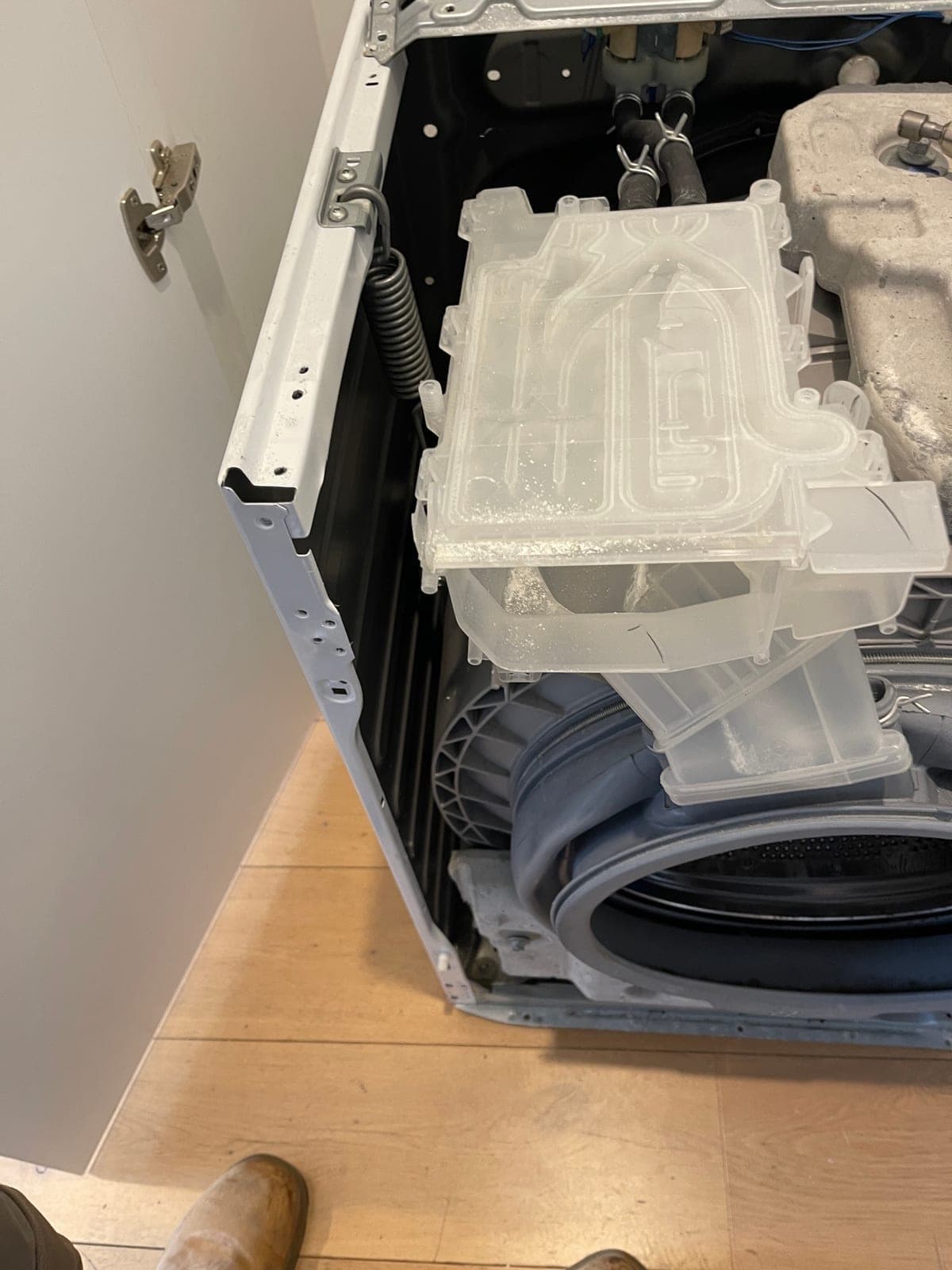 A washing machine opened up, showing the dispenser assembly and hoses.